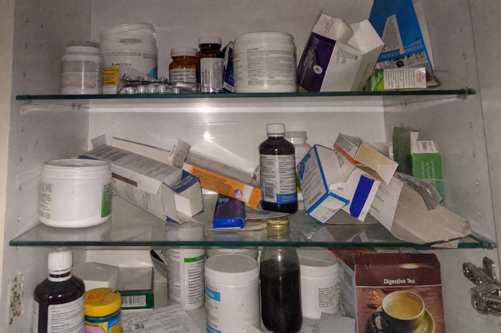 An open bathroom cabinet crowded with laxative boxes and supplement bottles